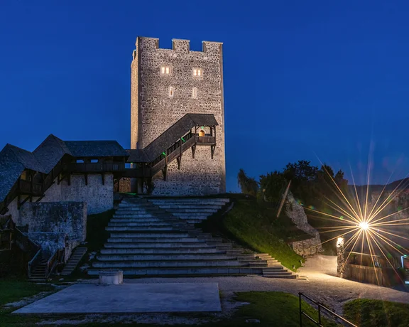 Medieval stone tower and steps illuminated at dusk with a bright streetlamp nearby.