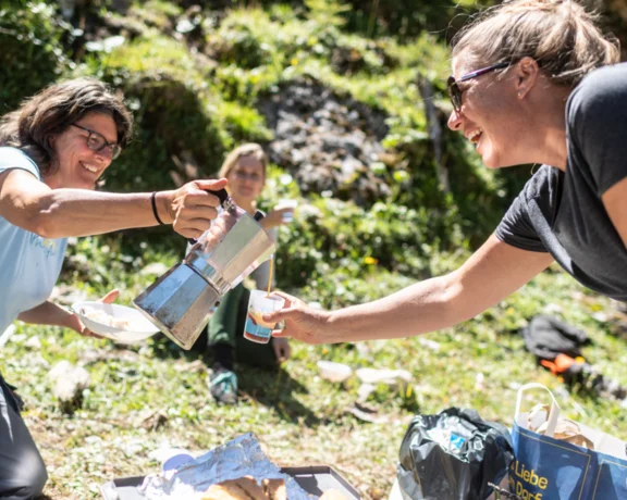 Two women laughing and pouring coffee outdoors during a picnic.
