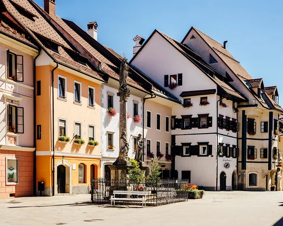 Colorful European buildings with flower boxes, a stone monument, and a clear blue sky.
