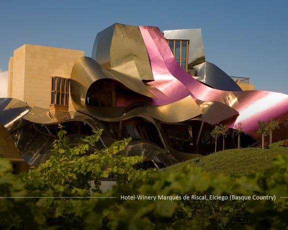 Modern building with metallic, wavy roof panels and bright pink accents surrounded by greenery.