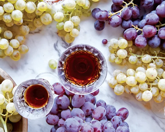 Red and white grapes with glasses of red wine on a marble surface.