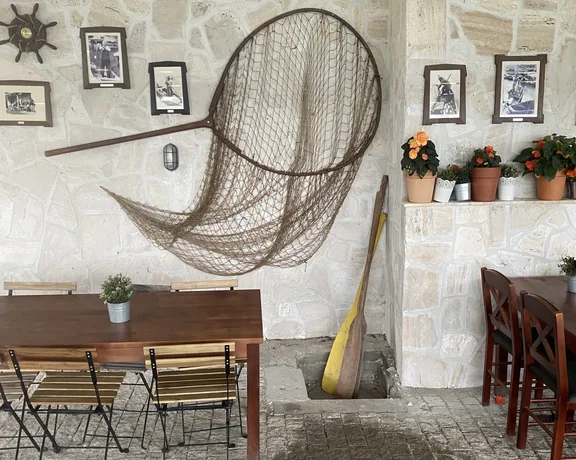 Cozy patio with tables, chairs, nautical decor, hanging net, and potted flowers on a stone wall.