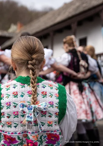 Girl with braided hair in a colorful embroidered vest watching a traditional folk dance.