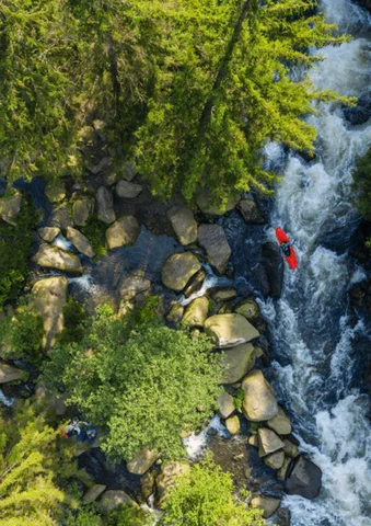 Red kayak navigating a rocky river surrounded by lush green trees.