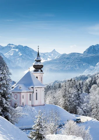 Snow-covered church with mountains in the background under a clear blue sky.