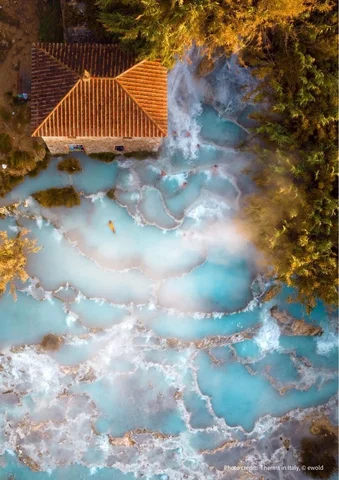 Thermal springs with turquoise water and steam beside a rustic building, surrounded by trees.