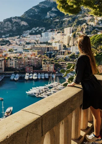 Woman overlooking a marina with yachts and colorful buildings in a coastal city.