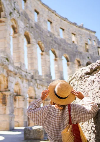 Person with a straw hat admiring ancient stone ruins under a clear blue sky.