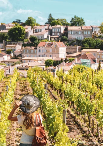 Woman in a vineyard looking toward a hillside village under a clear blue sky.