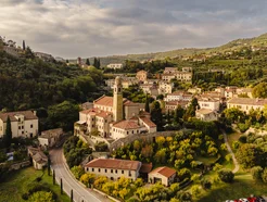 Hilltop village with historic buildings surrounded by green trees under a cloudy sky.