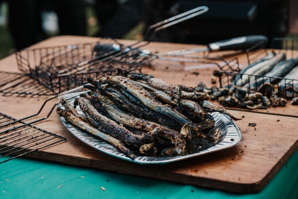 Grilled smelt fish stacked on a plate at the Smelt Festival in Narva-Jõesuu, Estonia, with barbecue racks in the background.