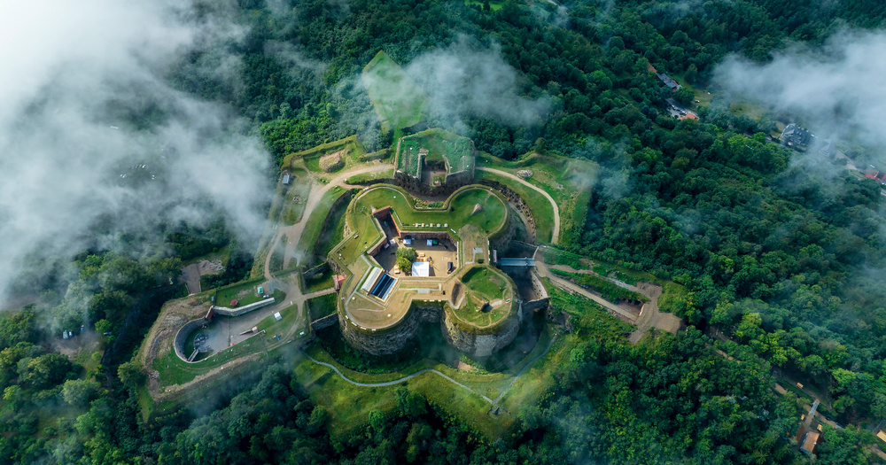Srebrna Gora Castle seen from above, surrounded by dense green scenery and a cloudy sky backdrop.