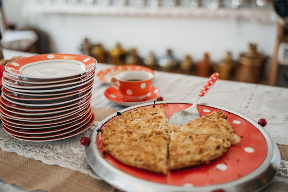 Traditional Estonian cabbage pie served on a polka-dot plate at Samovar House, accompanied by stacked plates and a cup of tea.