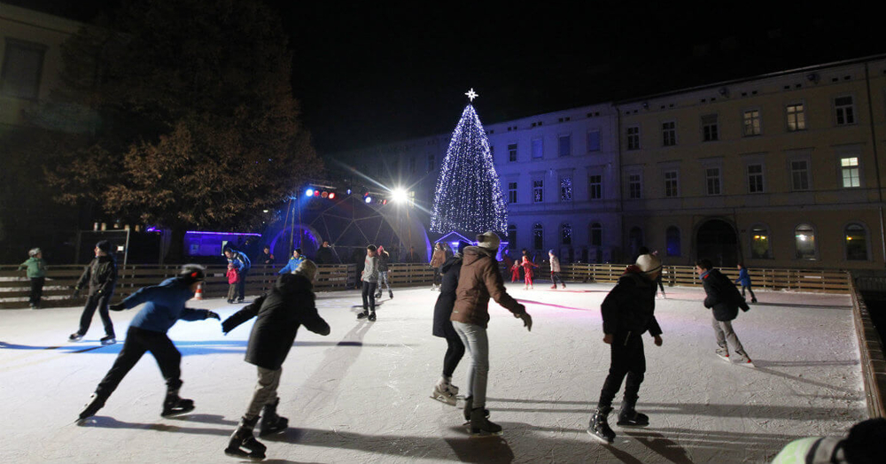 People ice skating at night with a lit Christmas tree in the background.