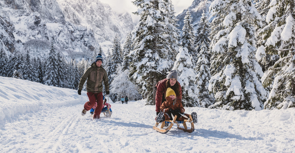 Children play with sleds in a snowy forest landscape in Slovenia.