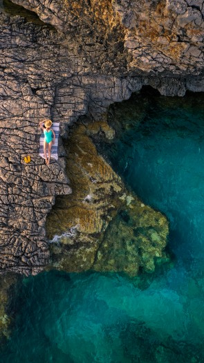 A woman sunbathing on rocky cliffs beside the crystal-clear turquoise waters of Cape Veslo, Montenegro.