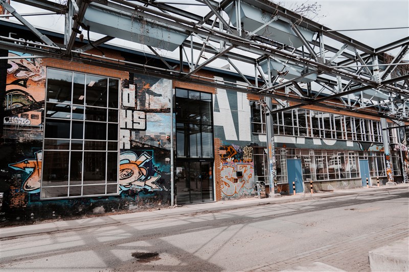 Piet Hein Eek facade adorned with vibrant graffiti art, large windows, and industrial elements under a steel framework.