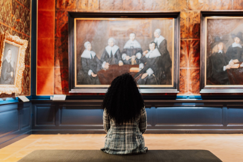 Woman seated in the Frans Hals Museum in Haarlem, Netherlands, looking at the famous painting Regentesses of the Old Men's House.