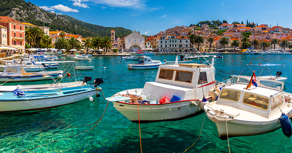 Boats anchored in the turquoise harbour of Hvar Town, Croatia, with historic buildings and palm trees in the background.