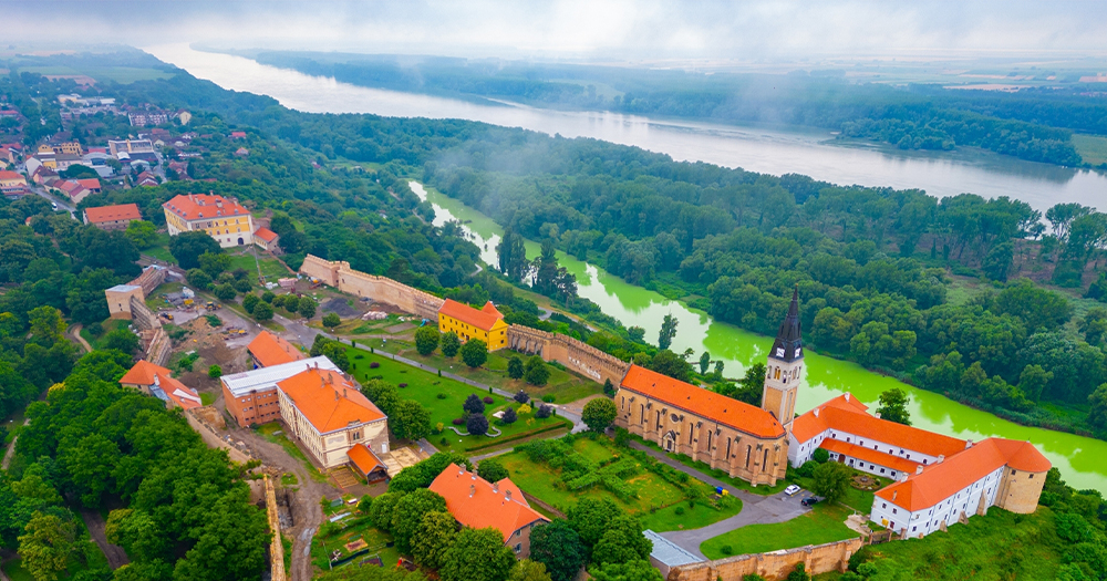 Ilok old town and fortress overlooking the Danube River, surrounded by greenery and vineyards.