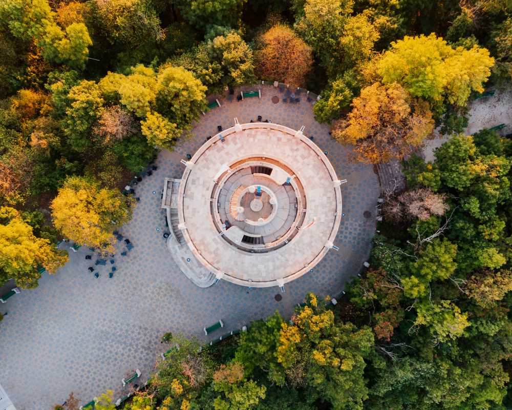 Aerial view of the circular Erzsébet Lookout tower surrounded by green and autumn-coloured trees.