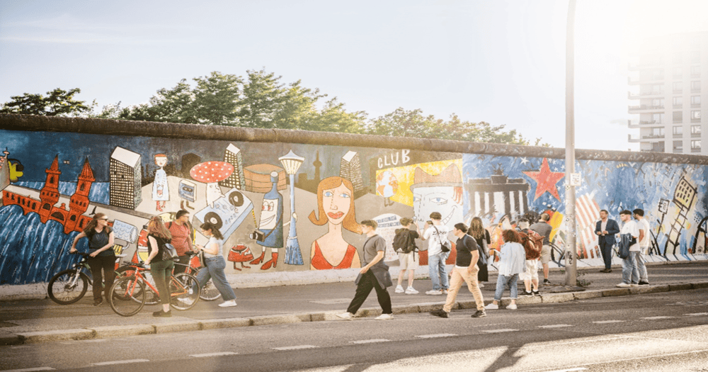 Sunlit East Side Gallery in Berlin with people walking along the open-air mural gallery on a clear day.