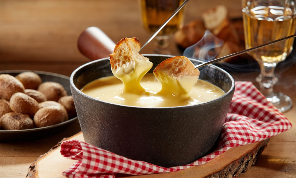 Traditional Swiss cheese fondue served with pieces of bread and a glass of wine on a red checkered tablecloth.