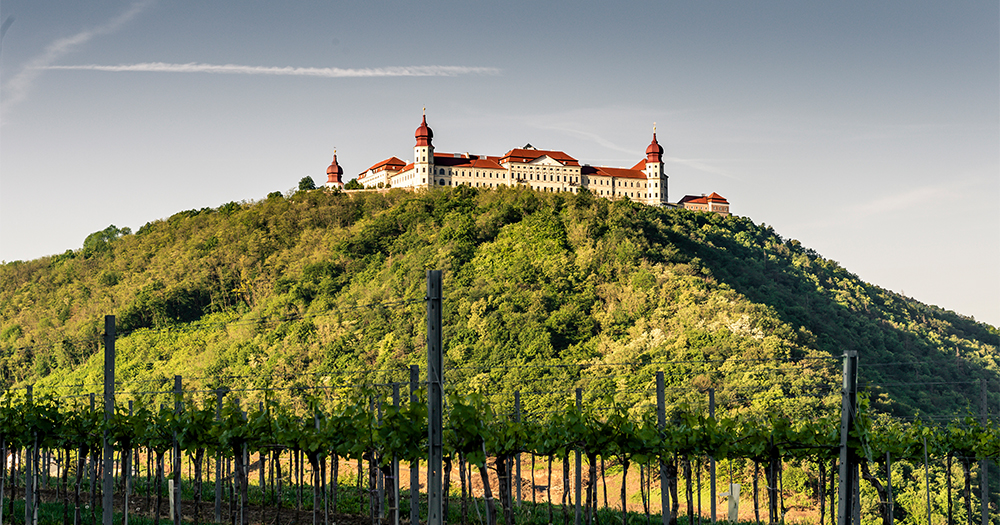 Aerial view of Göttweig Abbey on a sunny day, surrounded by lush green vineyards and forested hills.