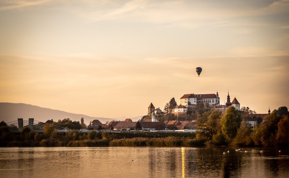 Ptuj Castle overlooking the town at sunset with a hot-air balloon floating above the landscape in Slovenia.