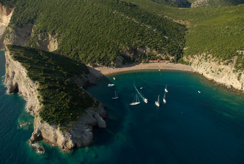Aerial view of Queen’s Beach, a secluded cove with yachts anchored in clear blue water near Budva, Montenegro.