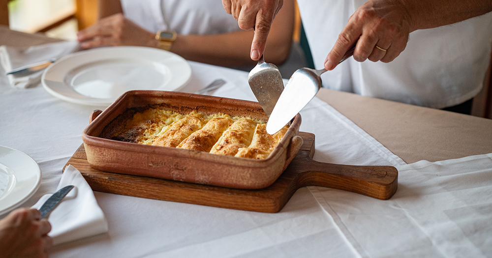 Close-up of traditional Croatian štrukli pastry being served hot from a baking dish at a dining table.