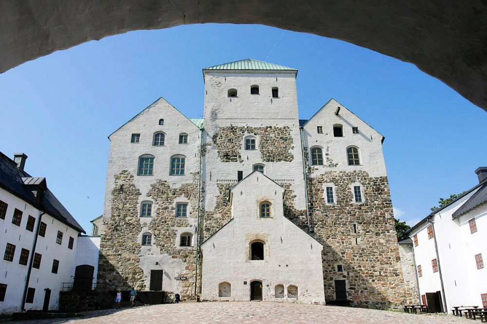 Front view of the medieval Turku Castle on a sunny day, showing its stone walls and towers against a bright blue sky.