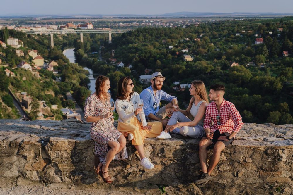 Overhead view of a group sharing wine, bread, cheese, and desserts on an outdoor terrace in Czechia.