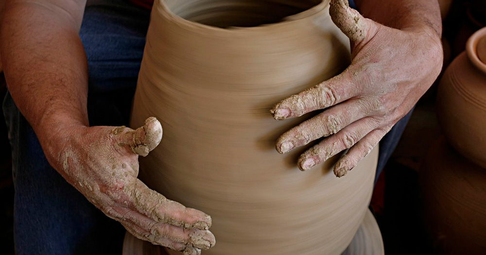 A potter shapes a spinning clay pot on a wheel, hands covered in wet clay, showcasing the artistry of ceramics.