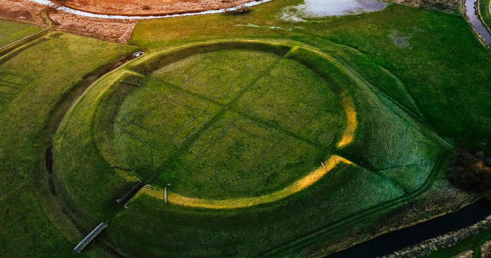 An aerial view of the Trelleborg Viking ring fortress in Denmark, showing its distinct circular earthen ramparts and internal cruciform layout marked on the grassy field.