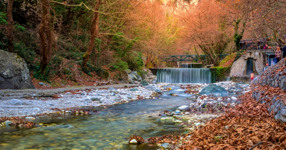 Autumn scenery at the Pozar Hot Springs in Greece, a stream, colorful leaves, and a footbridge.