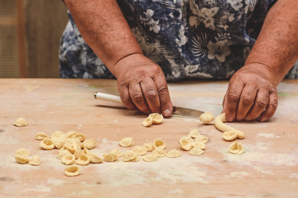 Hands cutting and shaping homemade pasta on a floured wooden surface.